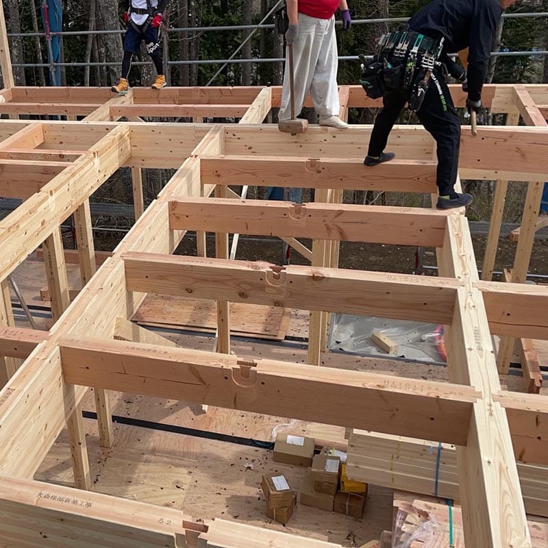 木造住宅建築現場の新築フレーム組立工事の作業風景。職人が安全装備で作業し、木材を組み立てている様子。株式会社エフ・アール・シーが施工する木造建築の進行中の様子。.